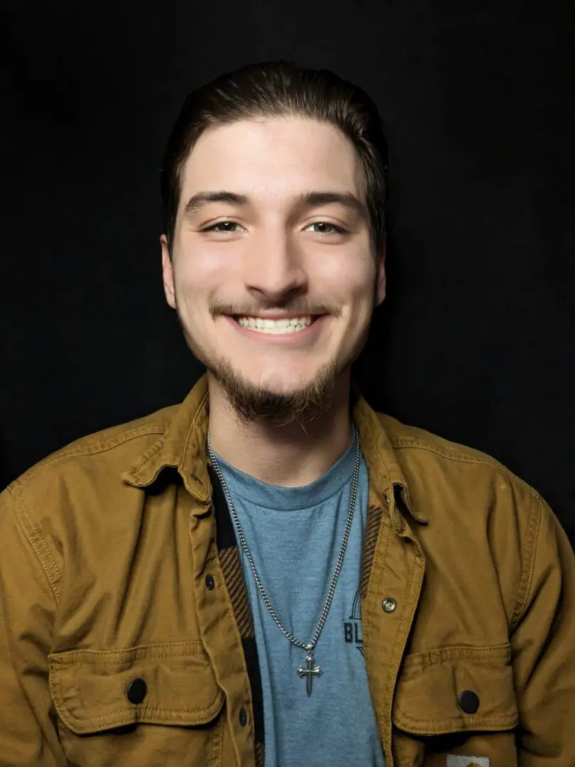 A man smiling for the camera in front of a black background.